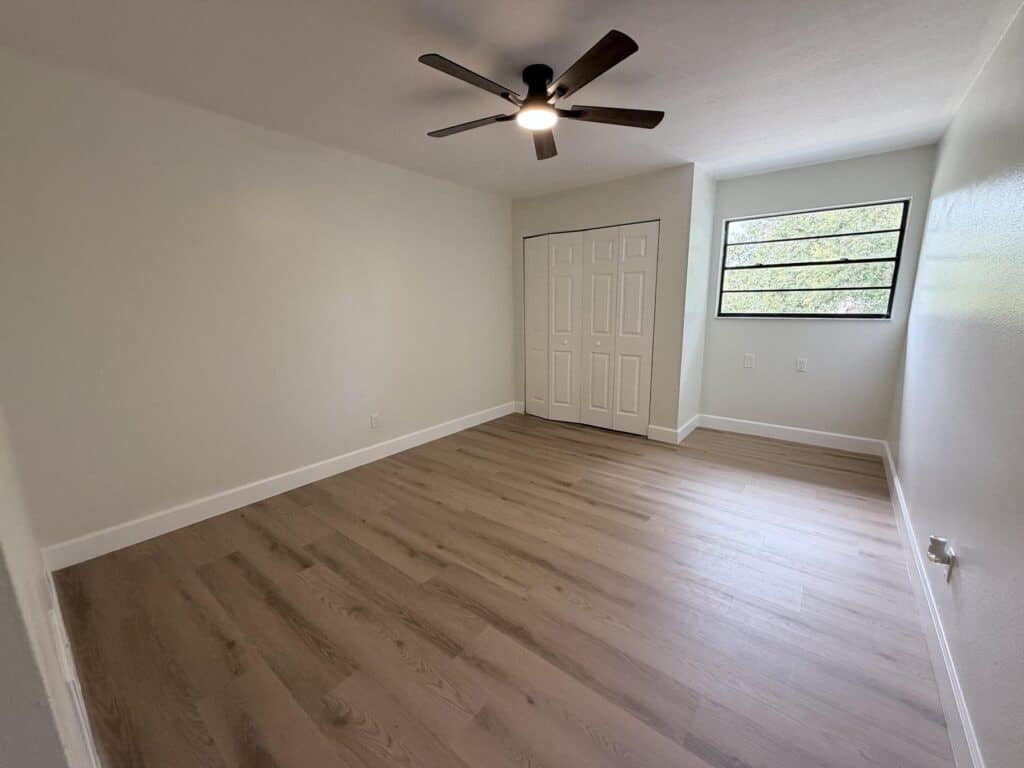 Flooring contractor Tampa Bay: warm oak plank bedroom floor with white baseboards